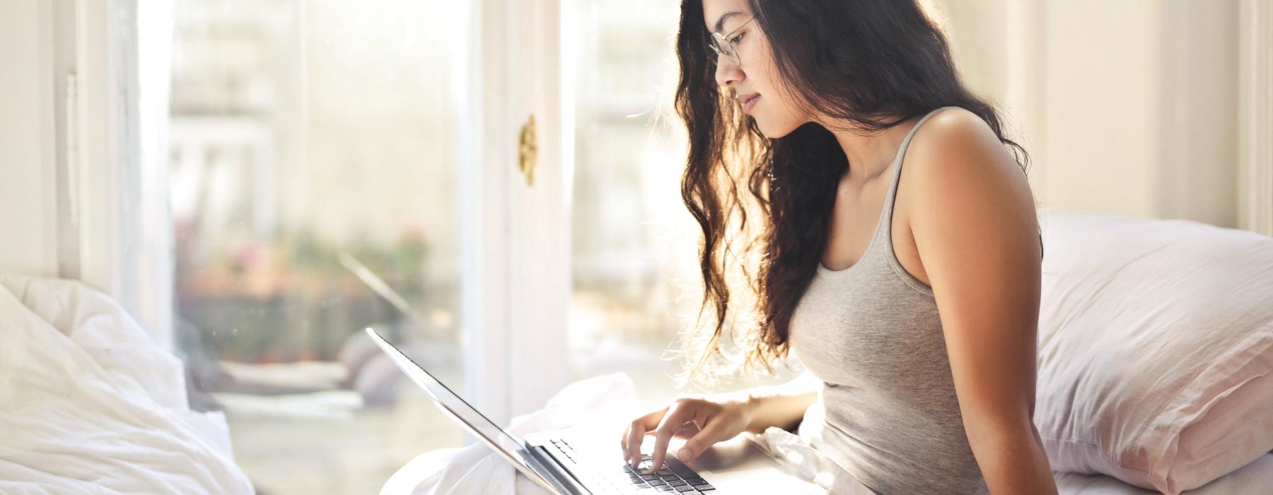 a woman sitting on a bed using a laptop